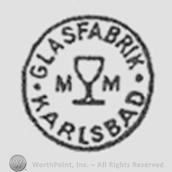A glass between two initials "M", "M". "Glasfabrik Karlsbad" written around, inside a circle