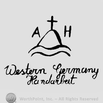 A bump above a wavy line with a cross above and the initials A H and the text Western Germany Handarbeit