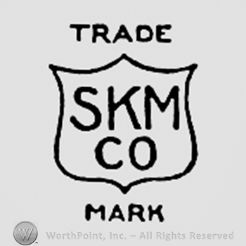 Letters SKM CO written on a shield; TRADE MARK written above and bellow.