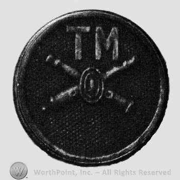 Insignia consisted of crossed cannons and a bullet at the intersection; letters TM above; all on a disc.