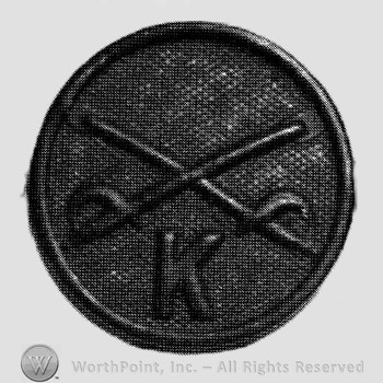 Disc with crossed sabres and letter K below.