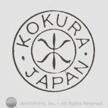 A double circle with the words Kokura and Japan between the circles and a form similar to a fleur-de-lis in the center