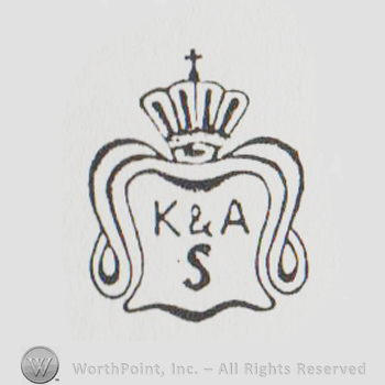 A crown with cross above a shield with uppercase K&A over uppercase S